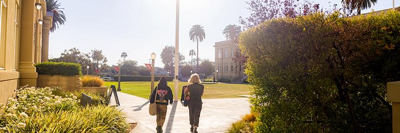 two women silhouetted walking on campus with the sun in front of them